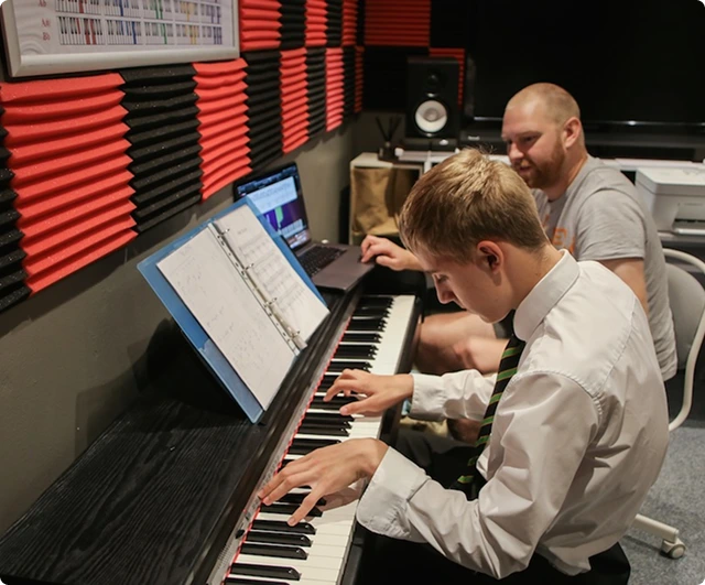 A child playing an electric piano, a teacher is sat next to them