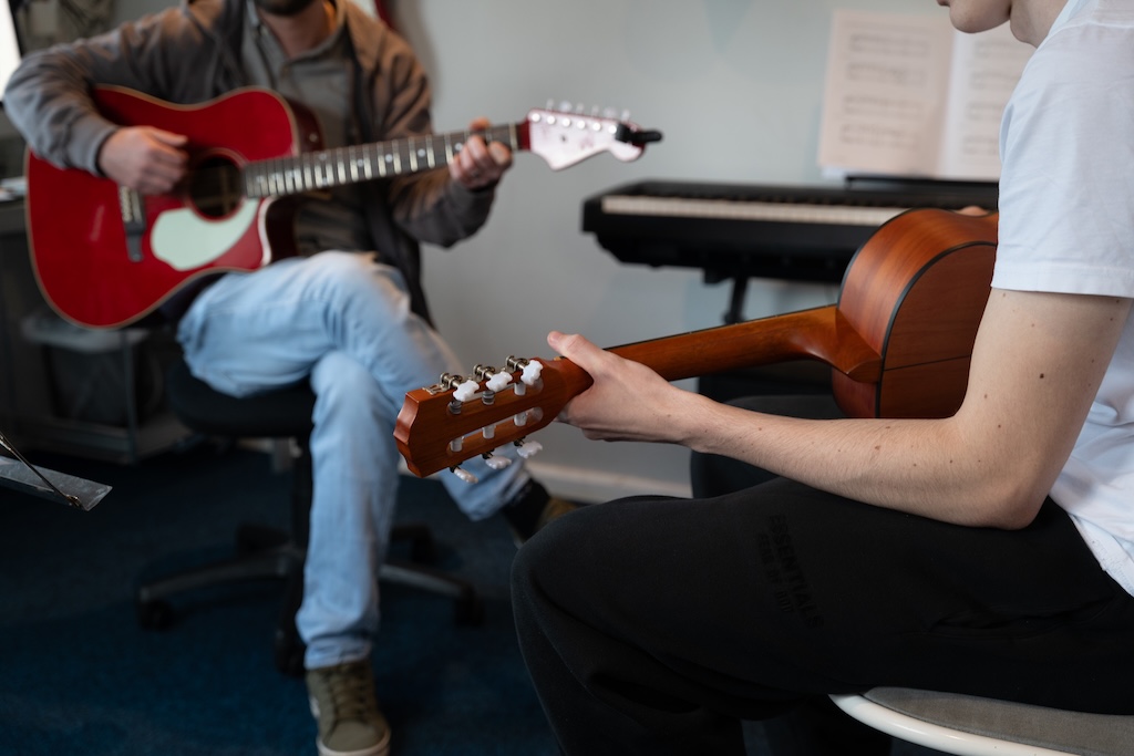 Two people sitting down playing guitars.