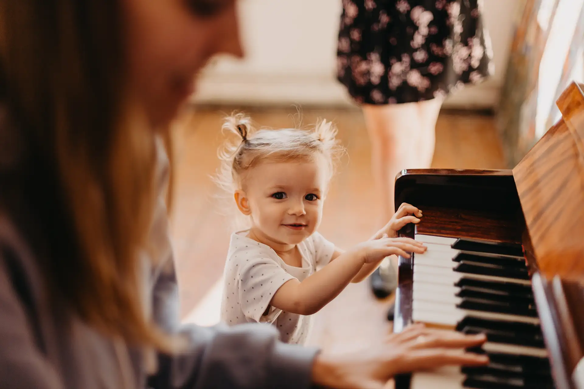 A young child sitting at a piano, playing alongside an adult